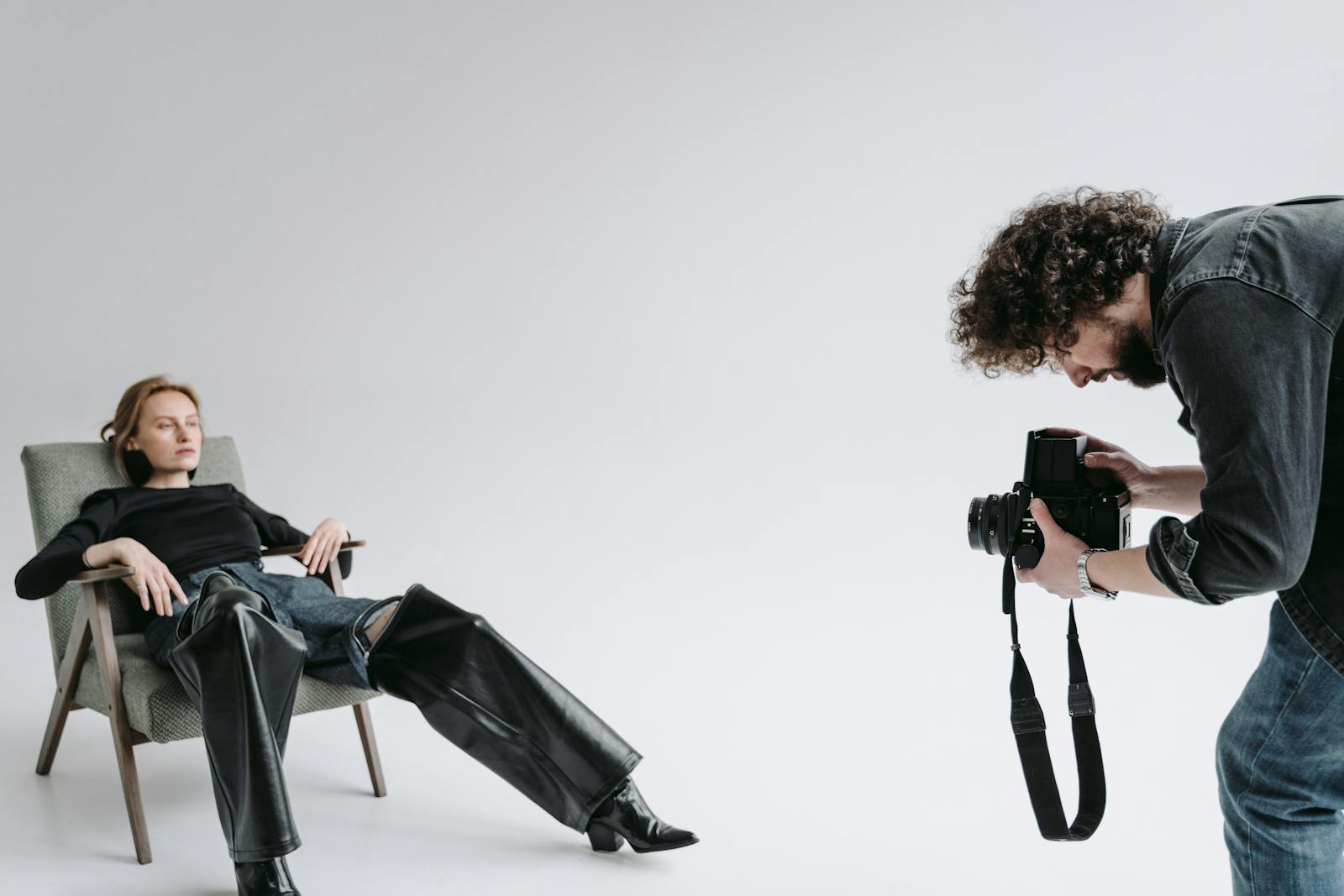Woman posing in studio while photographer captures with vintage camera.