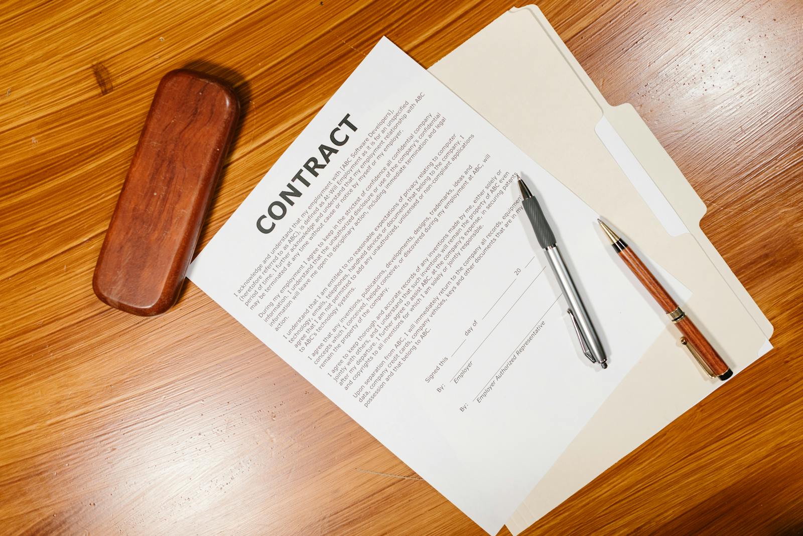 High-angle view of a contract document with pens and a case on a wooden table.