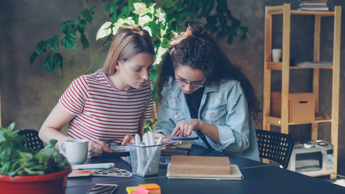 Two women collaborate on a project at a table.